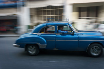Fototapeta na wymiar Habana, Cuba - 10 January, 2017:old blue car driving on a cuba street on a beautiful day with some people on the sidewalk