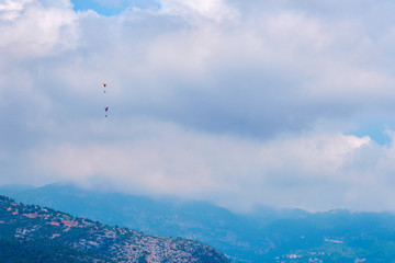 Fototapeta na wymiar Paragliders flying in blue cloudy sky over the mountains.