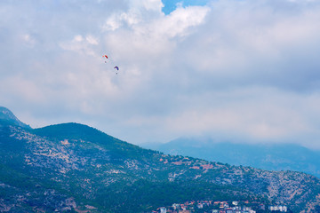 Paragliders flying in blue cloudy sky over the mountains.