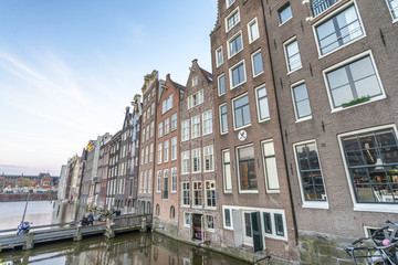 Fototapeta na wymiar AMSTERDAM, THE NETHERLANDS - MARCH 2015: View of city buildings along canal. The city hosts 15 million tourists annually