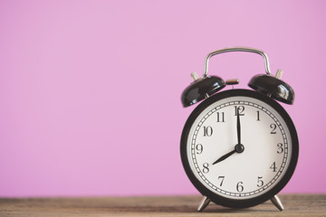 Retro alarm clock on wooden table with pink background, vintage style