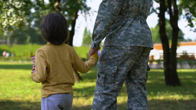 Military man and boy with national flag walking together in park, safe future