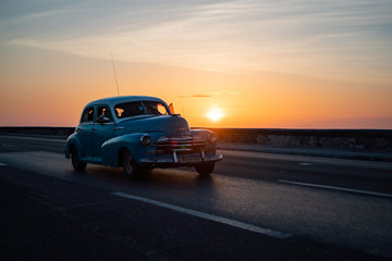 Fototapeta na wymiar Blue Vintage American Car in Havana Cuba during Sunset on Malecon Highway with Sea Wall next to the Ocean.