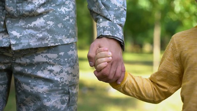 Serviceman holding boys hand, army defending safe future, family togetherness