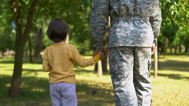 Armed forces soldier holding son hand and walking together in park, family love