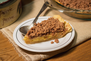 white plate with an apple pie slice  on a wooden background, a vintage spoon and a brown cloth 