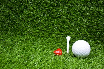 Golf ball and tee are on green grass background