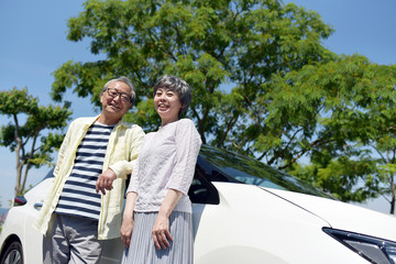 車の横に立つ笑顔のシニアカップル