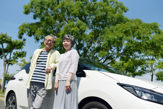 車の前に立つ笑顔のシニア夫婦