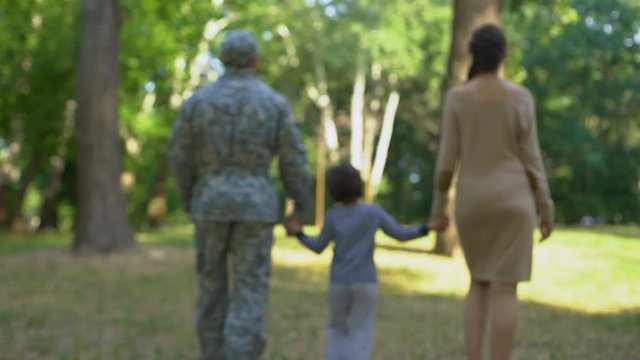 Military father with son and wife walking in park, holding hands, back view