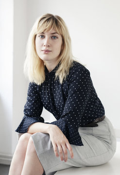 A relaxed portrait of a young blonde woman sitting on a desk.