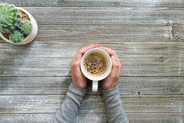 Person holding a coffee mug on a wooden desk overhead view
