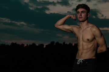 Young adult male flexing his muscles at twilight