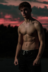 Fototapeta na wymiar Young adult male flexing his muscles at twilight