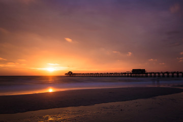 Fototapeta na wymiar Iconic Naples Pier the symbol of this famous city in southwest Florida, USA. Amazing and calm ocean during sunset, cloudscape after a big tropical storm in the Gulf of Mexico, close to Everglades Nati