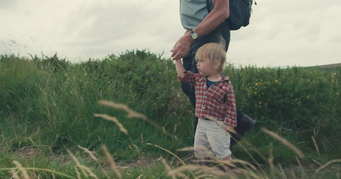 Little toddler walking on moor with his grandfather