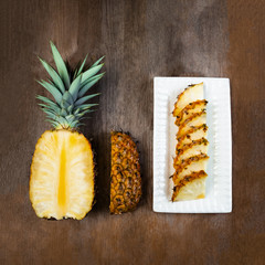 Pineapple fruit cut half, quarter and wedges and  displayed on white plate and wooden background. Square Composition. Juicy organically grown ripe and sweet