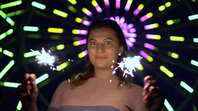 A beautiful girl with long hair holds fireworks in her hands against the backdrop of multicolored lights. slow motion