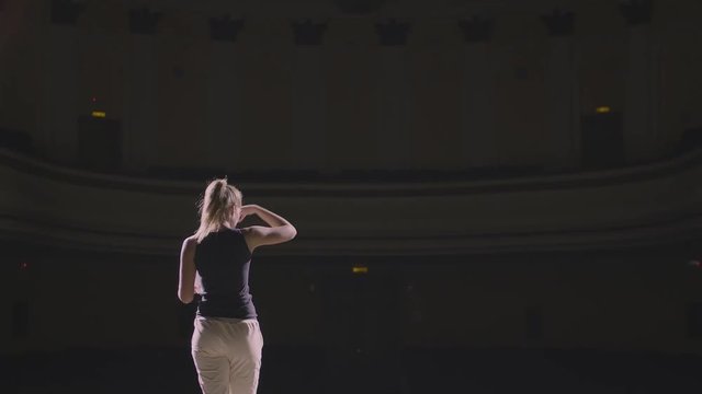 Adult girl walking on the theatre stage and do rehearsal before the premiere. At background empty hall with many rows of seats. The actress concentrated on the script and ready her self for acting