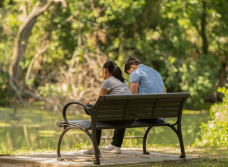 unknown couple take a break to relax on a park bench under a shady tree on a hot summer day