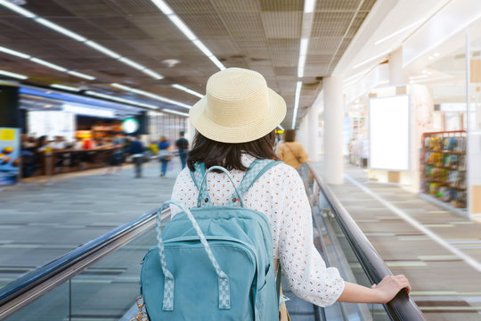 Beautiful young tourist girl wearing cream hat with green backpack on speedwalk in international airport to travel on weekends,motion blur,Travel departure concept.