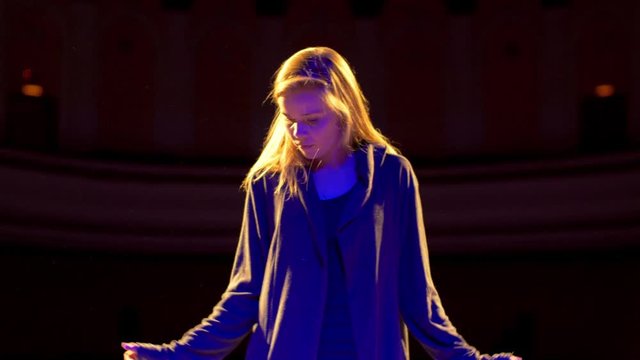 Pretty girl dancing at performance show on the stage under the blue soffits lights. Teenage female trendy dancer moving on the scene slow motion and carefully looking at the camera at rehearsal