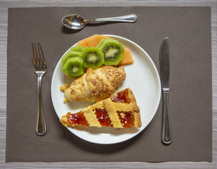 Breakfast: dish with home made jam tart, croissant, melon and kiwi fruit