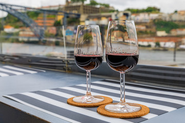 Glasses of port wine at an outdoor restaurant with the Douro river and Dom Luis I bridge blurred in the background in Porto, Portugal