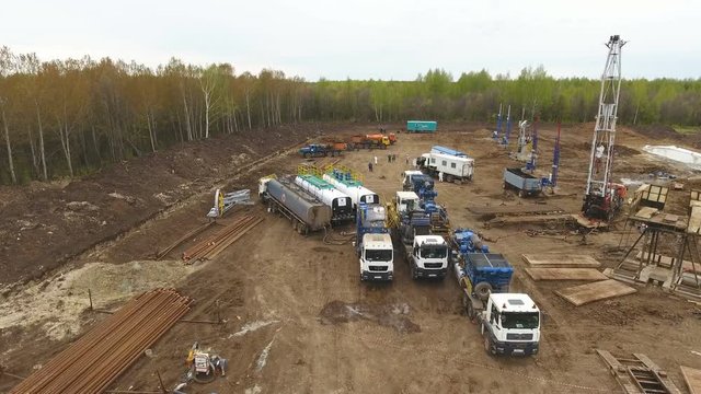bird-eye flight above site on brown territory with vehicles against birches