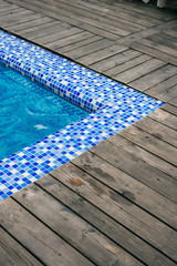 Bright blue swimming pool corner and wooden deck at hotel.