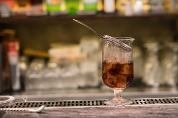 A glass with alcoholic cocktail standing on bar counter. Mixing alcohol drink process. Modern trends in club and bar industry. Selective focus on the glass. 