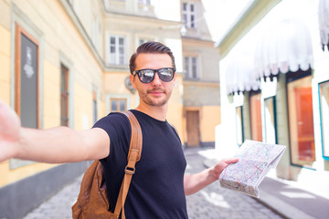 Fototapeta premium Man tourist with a city map and backpack in Europe street. Caucasian boy looking with map of European city.