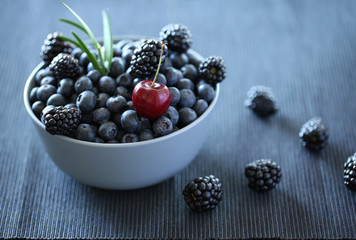 Blueberry, blackberry cherry and grass in a bowl isolated on blue background