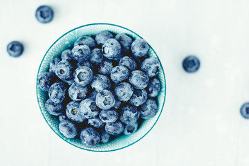 Top view of a blue bowl with fresh ripe blueberry over white background. The concept of healthy eating and lifestyle.
