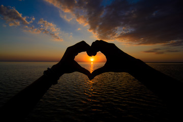 Gils` hands show а love symbol on sea sunset background