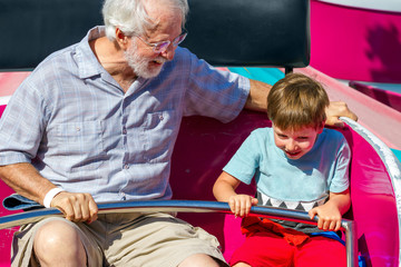An Elderly Man and His Young Grandson Ride on a Spinning Carnival Ride the Man is Looking at the...