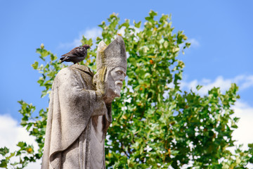 Paris, France - August 10, 2017. Statue of Saint Denis, the first bishop of Paris, martyr holding his head in hands by summer day on Montmartre hill park. Pigeon sitting on beheaded bishop's statue. - obrazy, fototapety, plakaty
