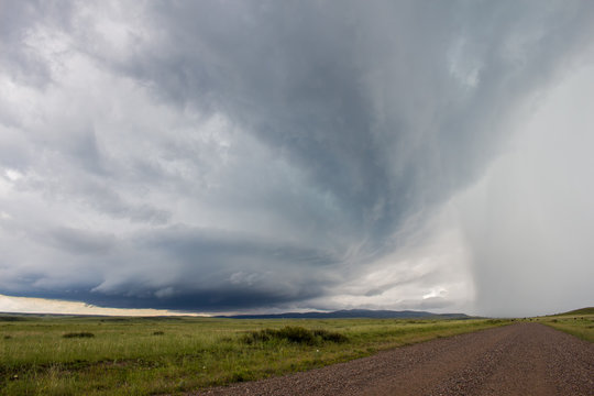 Looking down a gravel road at a supercell thunderstorm approaching with mountains on the horizon. © Dan Ross