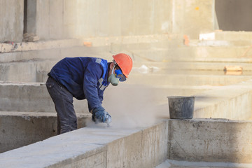 The worker in overalls and a protective mask grinds the concrete wall.