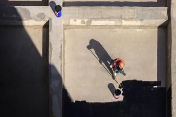 The worker in overalls applies an insulation coating on the concrete surface. View from above.