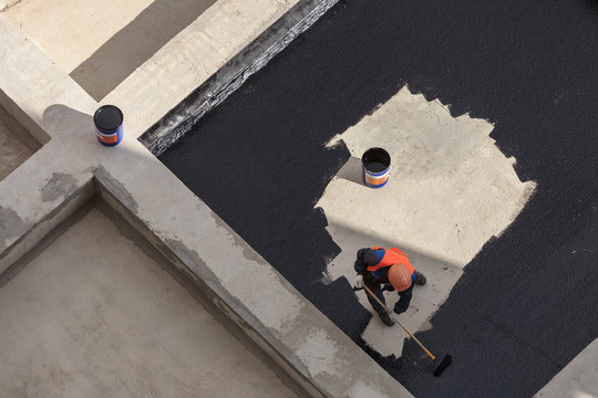 The worker in overalls applies an insulation coating on the concrete surface. View from above.