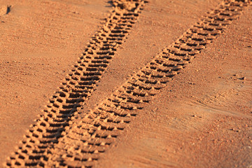 Traces of tire treads on orange sand, diverging in different directions.