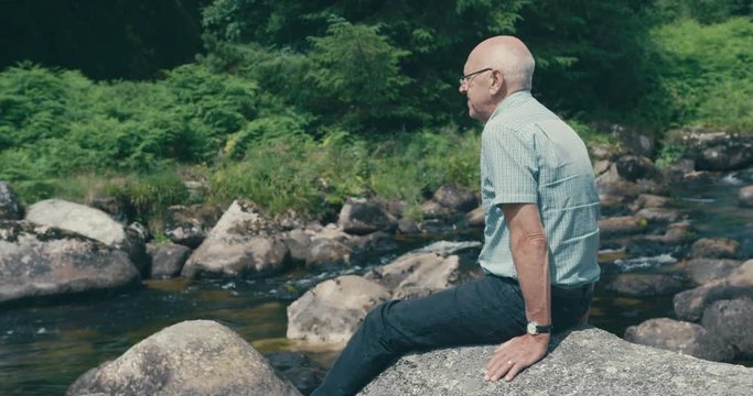 Senior man sitting on a rock in by the water in nature