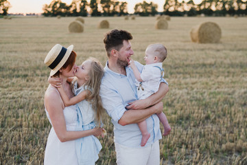 Happy stylish caucasian family, mother, father, daughter and son, walking together in summer wheat field. Mother and father playing with children outdoors. Love, parenthood, childhood, happiness.