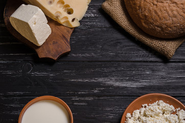 Rural breakfast. Bread, cheese, feta, cottage cheese and milk on a wooden black table.