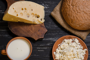 The rural breakfast. Bread, cheese, cottage cheese and milk on a wooden black table.