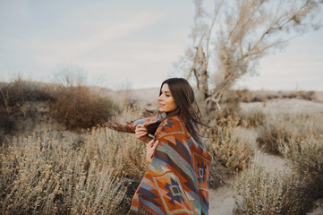 Back side of boho woman with windy hair in the desert nature, turning her head and smiling . ...