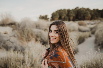Smiling beautiful hipster traveler girl in gypsy look in desert nature.  Artistic photo of young hipster traveler girl in gypsy look, in Coachella Valley in a desert valley in Southern California.