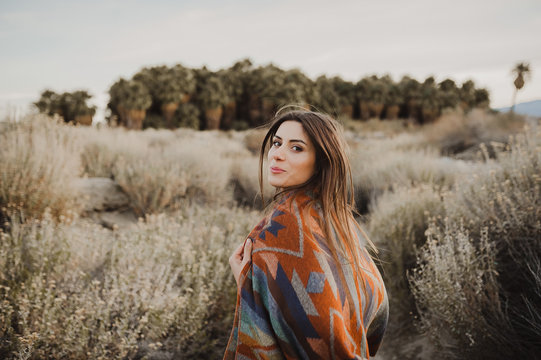 Back side of boho woman with windy hair in the desert nature, turning her head and smiling .  Artistic photo of young hipster traveler girl in gypsy look, in Coachella Valley in a desert vall