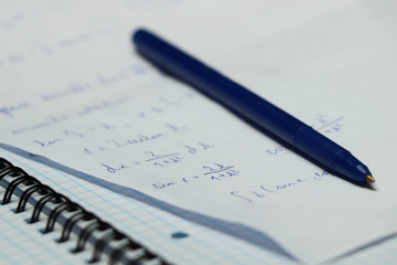 A blue pen with small exercise book and different make a calculation in math on university. A small...